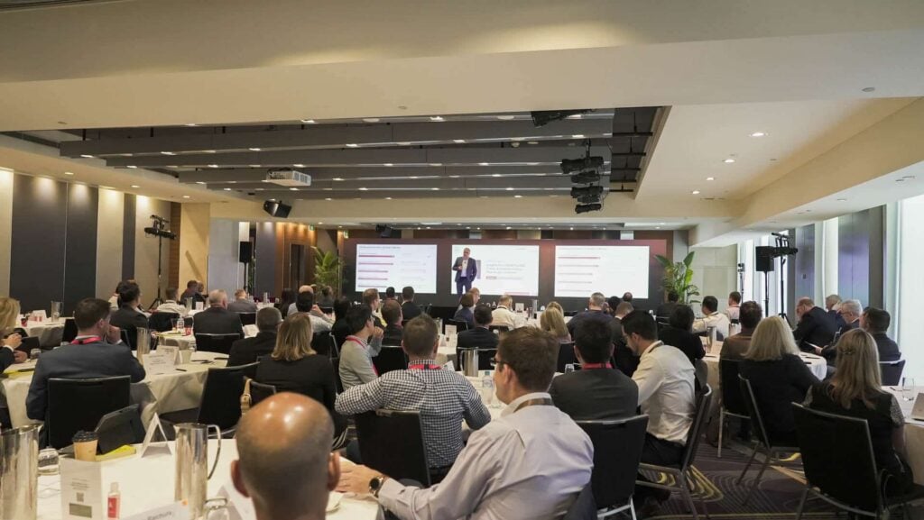 Conference attendees seated at round tables listening to a speaker presenting financial and business insights at The CFO Edge event