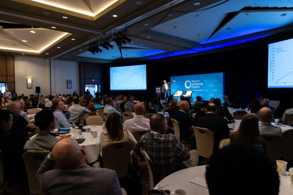 Attendees seated in a conference hall listening to a speaker presenting on stage at the Fall CFO Leadership Conference